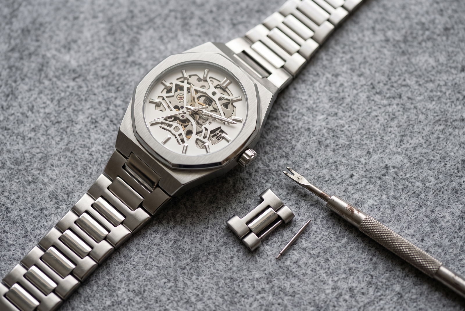 Overhead view of a LuxeShine Tempus steel watch bracelet with links separated and a spring-bar tool, illustrating how to resize a watch bracelet.